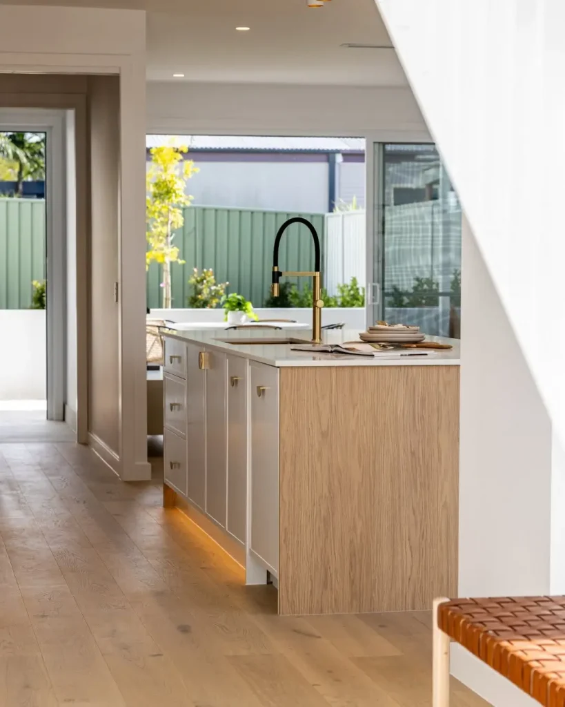 Bright modern kitchen with timber flooring, island bench, and brushed gold tapware.
