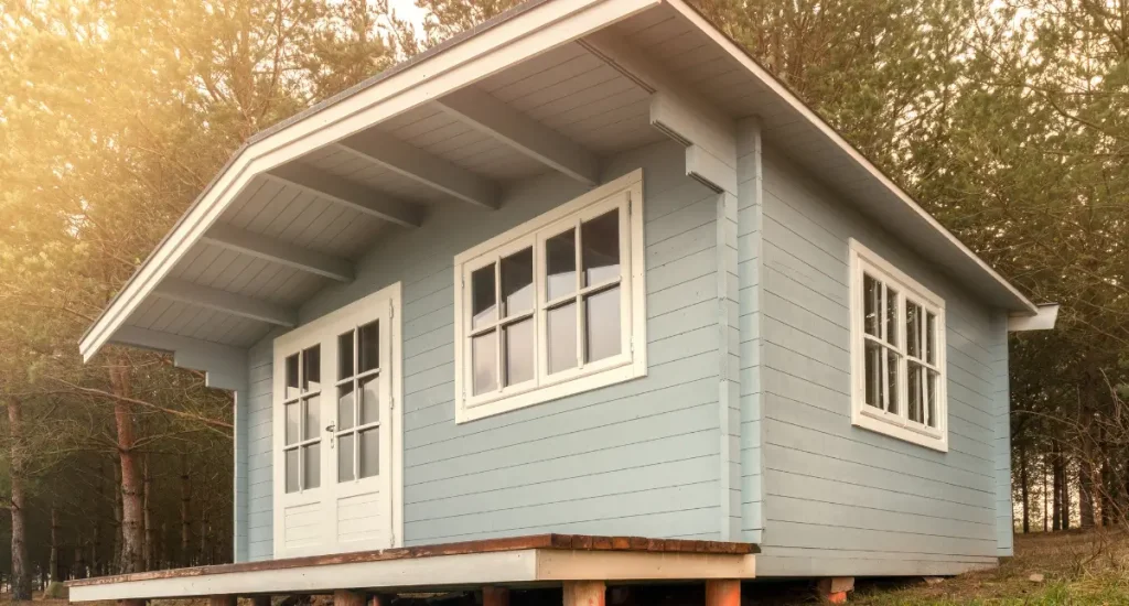 Modern timber granny flat with pitched roof, painted soft blue, elevated on stumps in a bushland setting.
