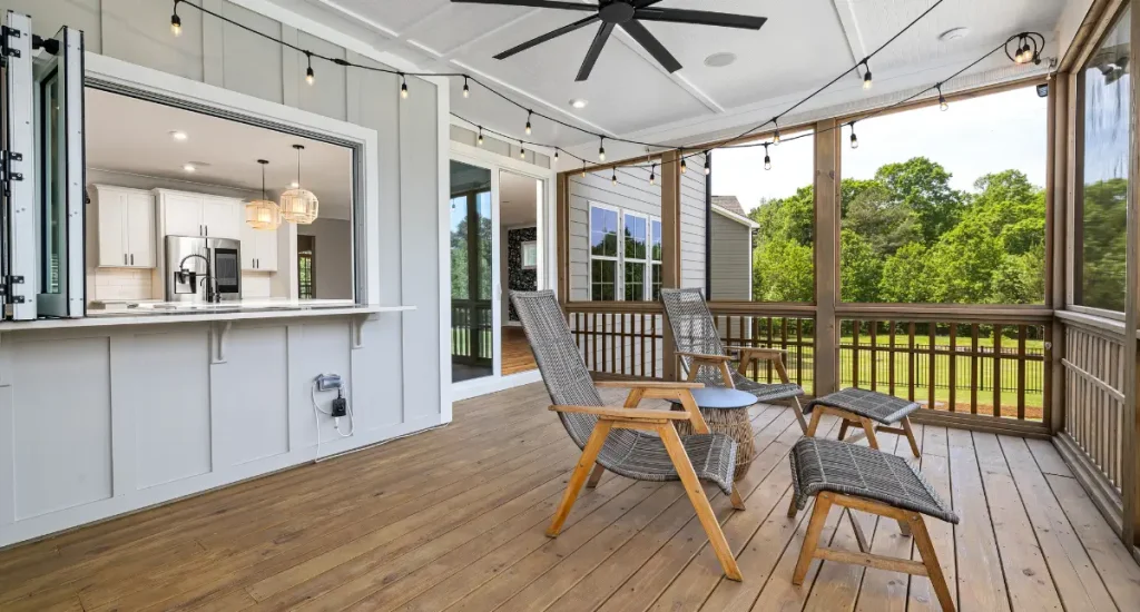 Modern timber deck with lounge seating, ceiling fan, and open window bar connecting to a white kitchen.