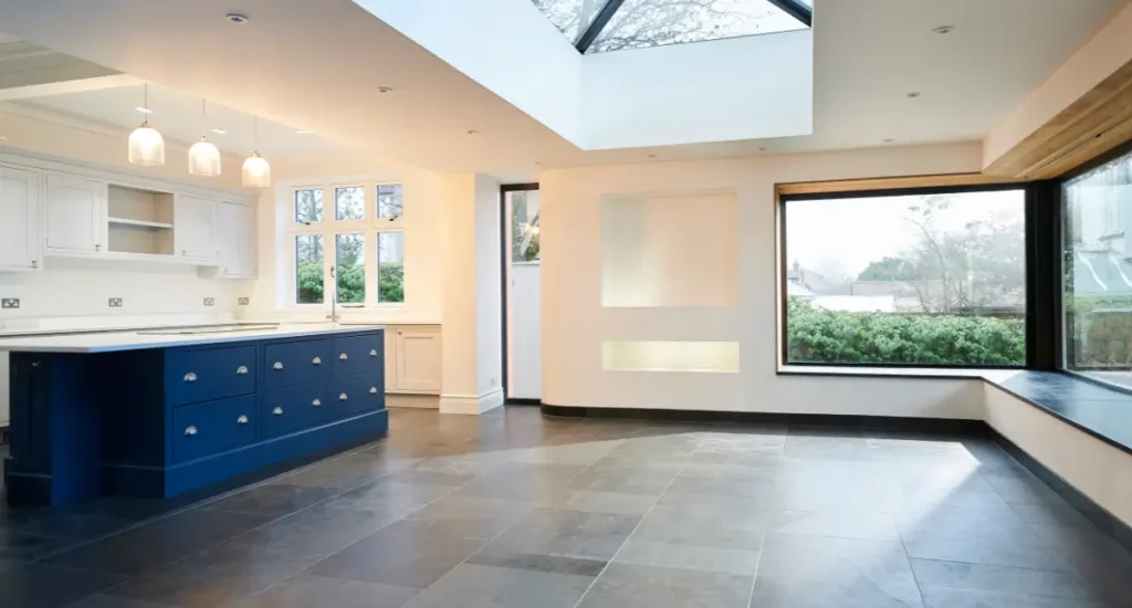Contemporary kitchen with a blue island bench, white cabinetry, and a large skylight over slate flooring.