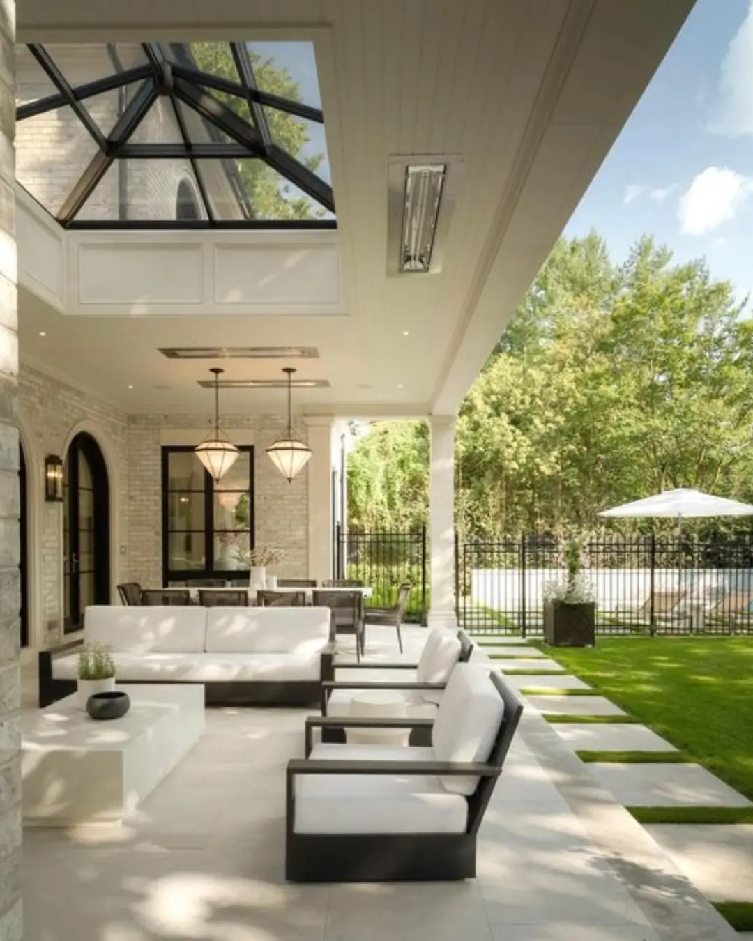 Modern outdoor living area with a skylight roof, white cushioned seating, and a view of the landscaped backyard.