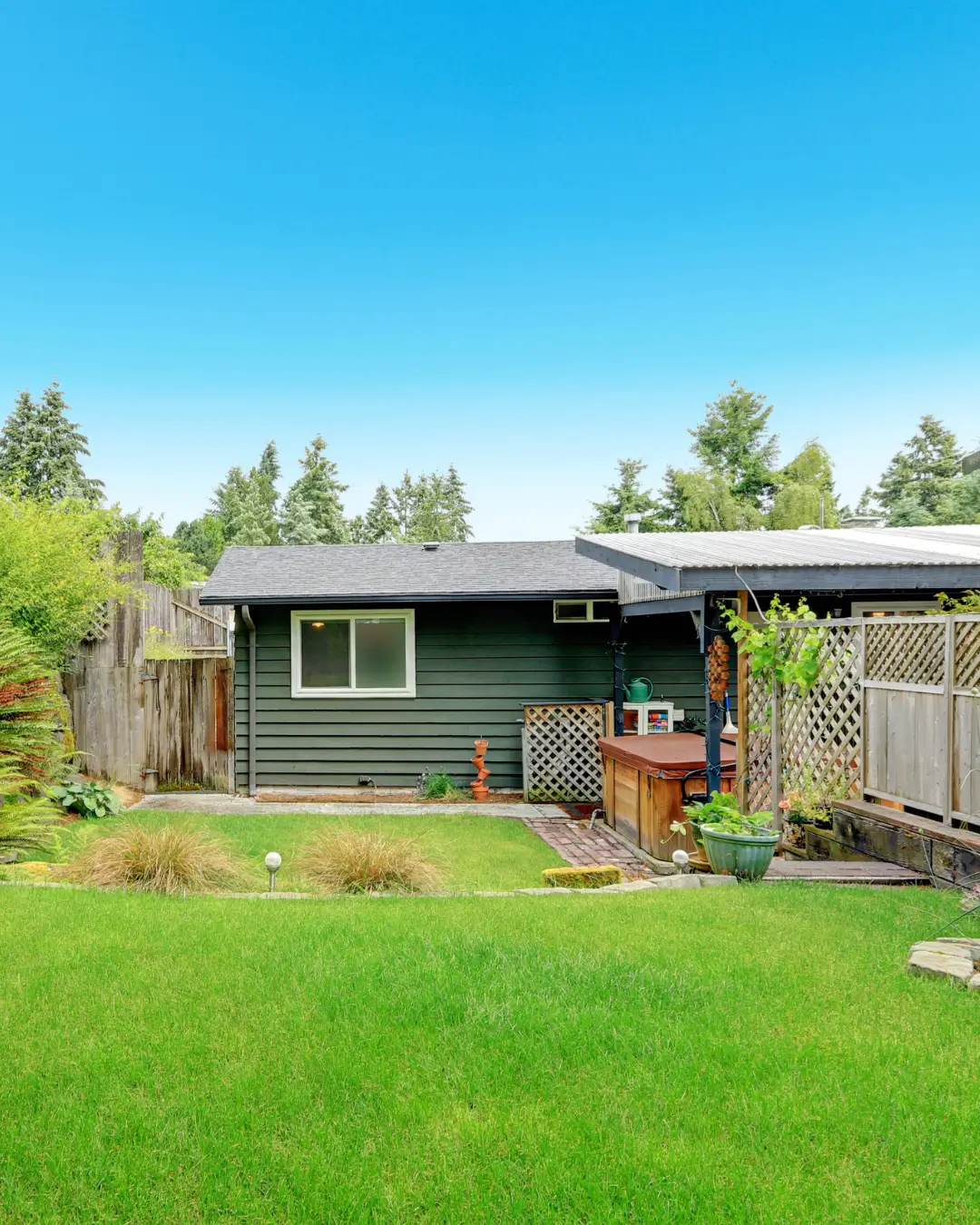 Backyard with modern granny flat and pergola beside landscaped garden and lawn.