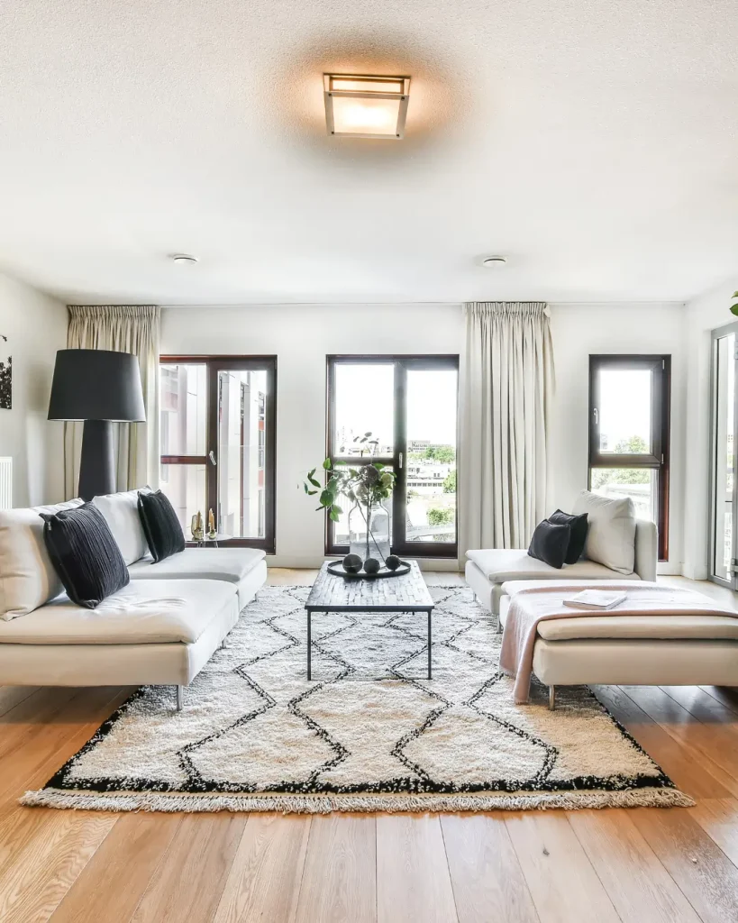Modern sunlit living room with neutral interiors, black accents, and full-length windows.