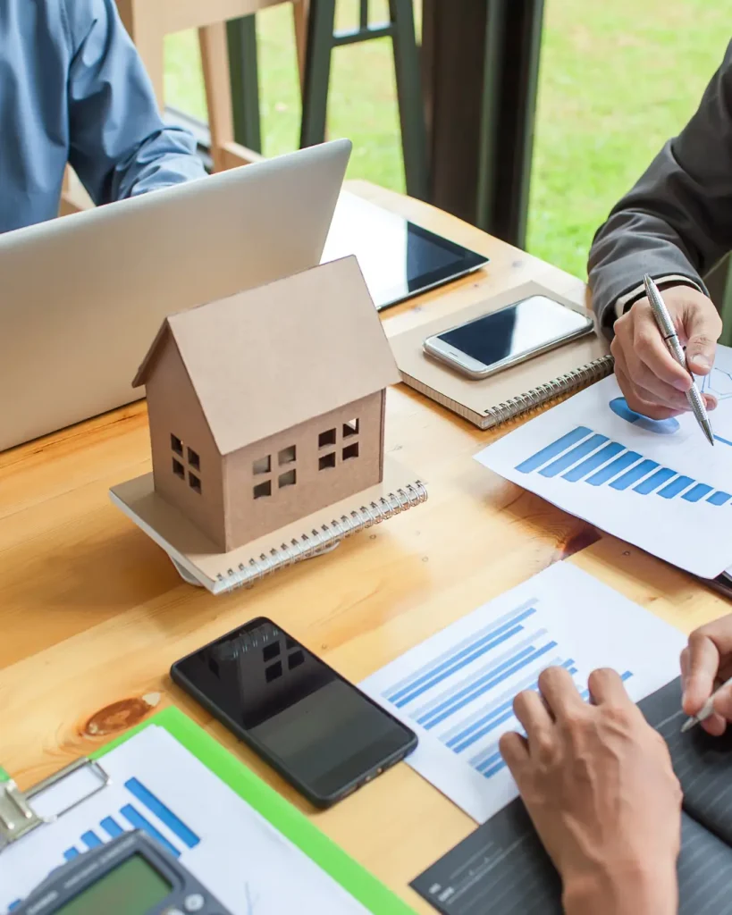 Team reviewing building plans and permit requirements for outdoor living projects beside a miniature house model.