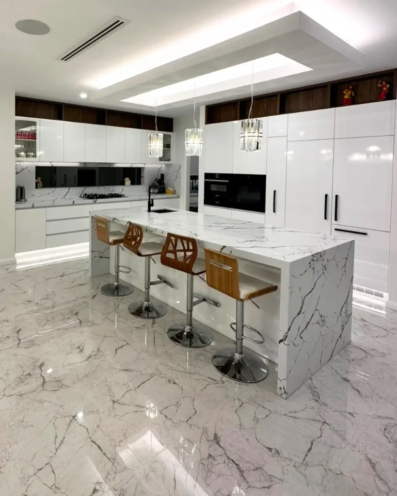 Modern luxury kitchen with marble flooring, white cabinetry, large island bench, and contemporary pendant lighting.