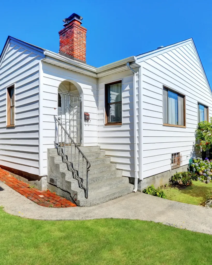White detached granny flat with brick chimney, front steps, and lush garden surroundings.