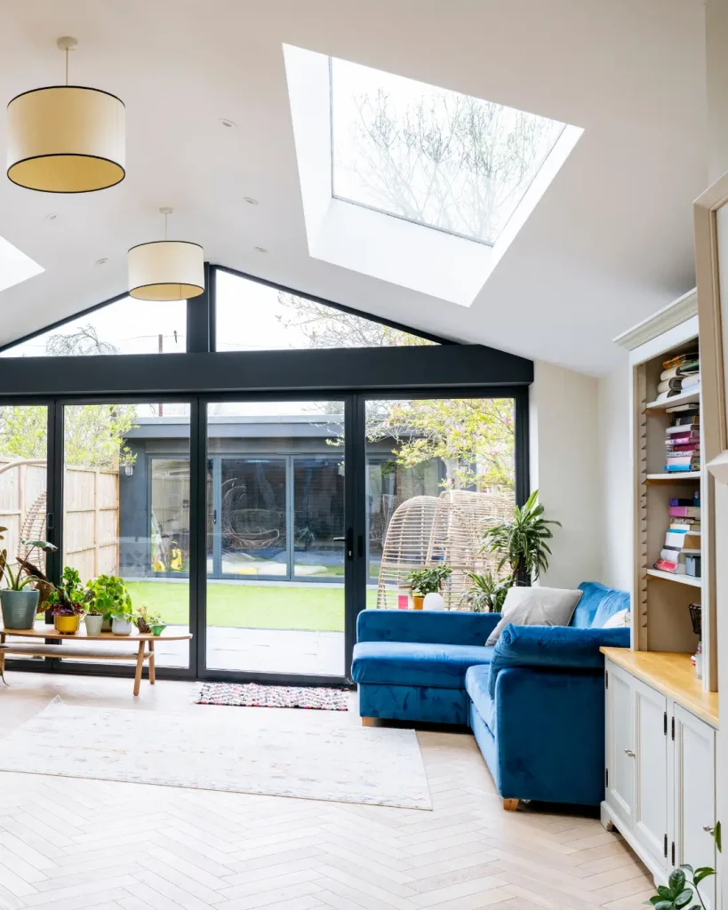 Bright living space with skylights, sliding glass doors, and a blue velvet sofa facing a landscaped backyard.