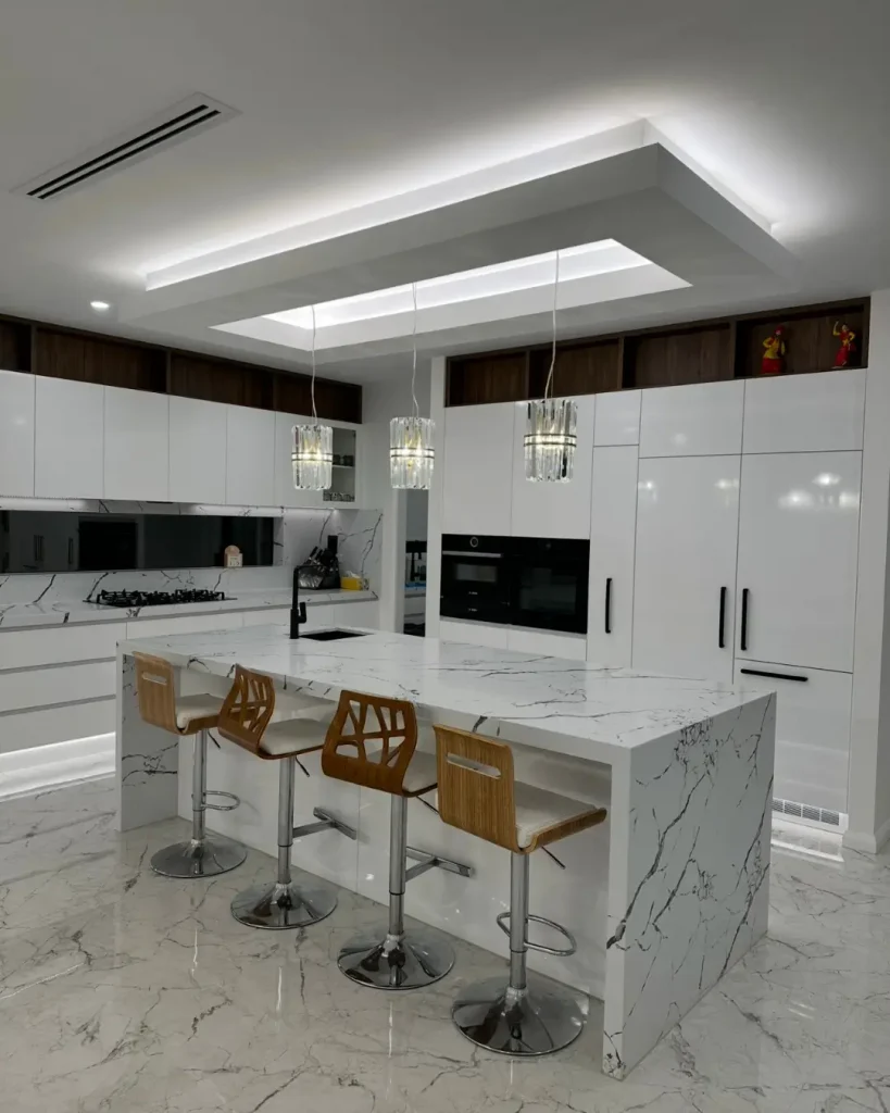 Luxurious white kitchen with marble island, pendant lighting, and integrated appliances.