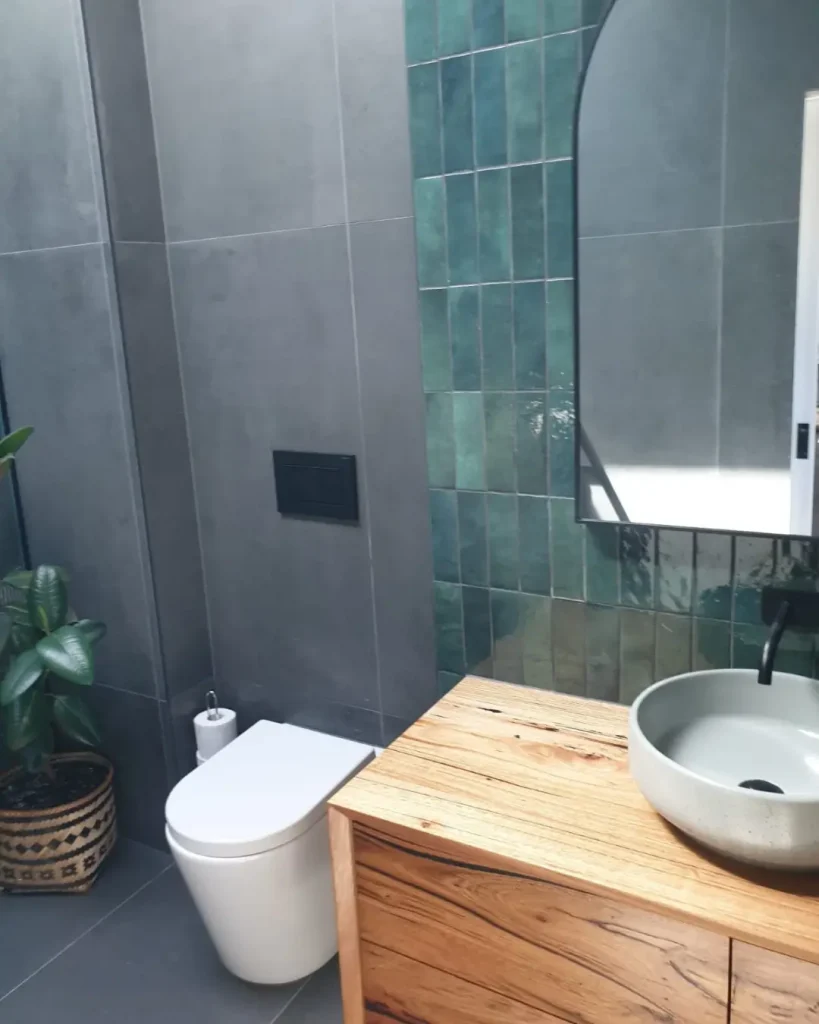 Modern bathroom with green feature tiles, wall-hung toilet, timber vanity, and round basin.