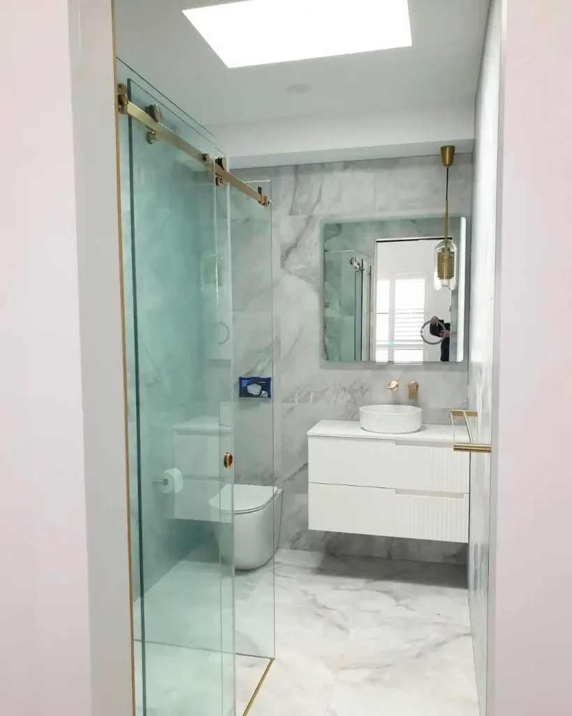 Modern bathroom with marble finishes, floating vanity, glass shower, and gold fixtures.