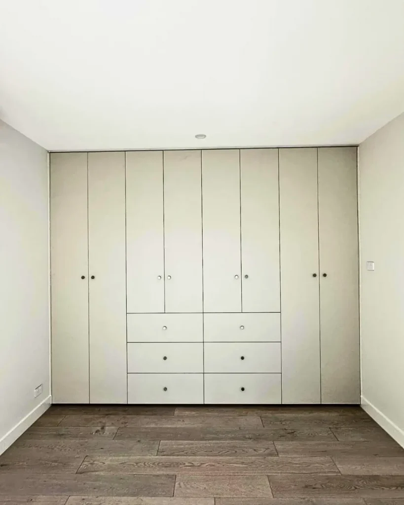 Minimalist built-in bedroom wardrobe with full-height cabinets and central drawers.