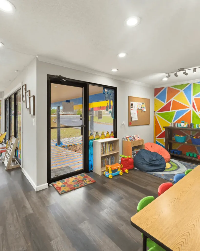 Bright and colourful childcare centre interior with play area, bookshelves, and wall art.