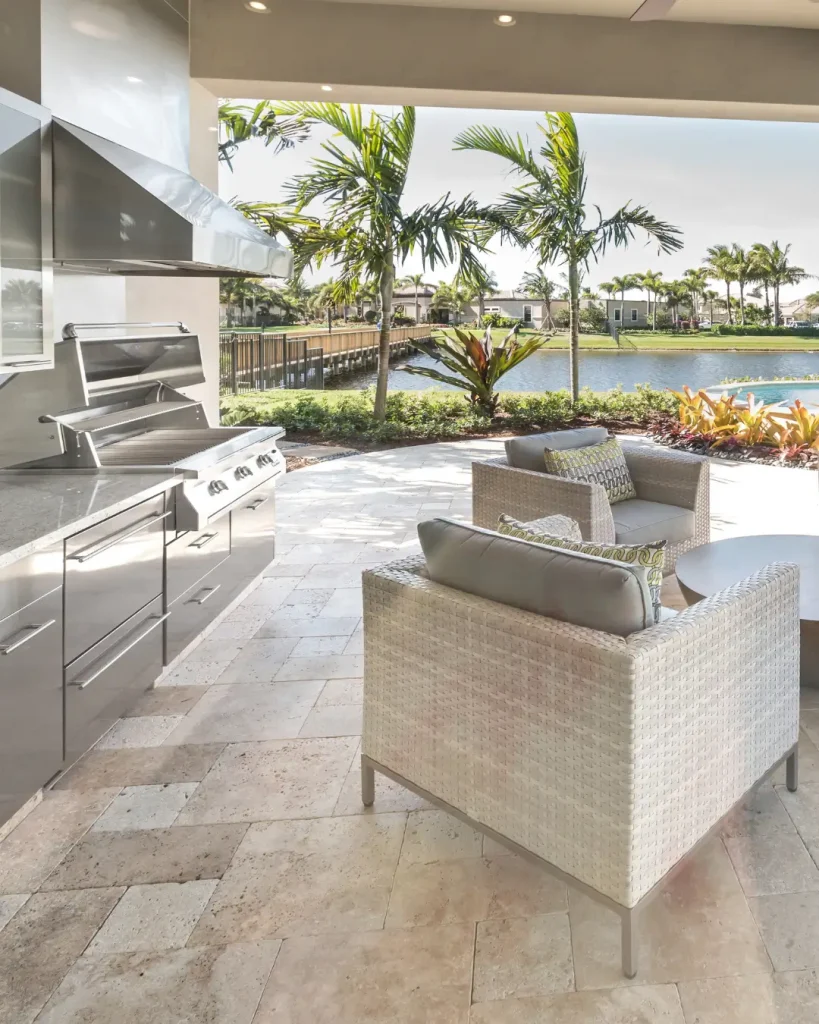 Luxury outdoor kitchen and seating area overlooking a waterfront with palm trees and tropical landscaping.