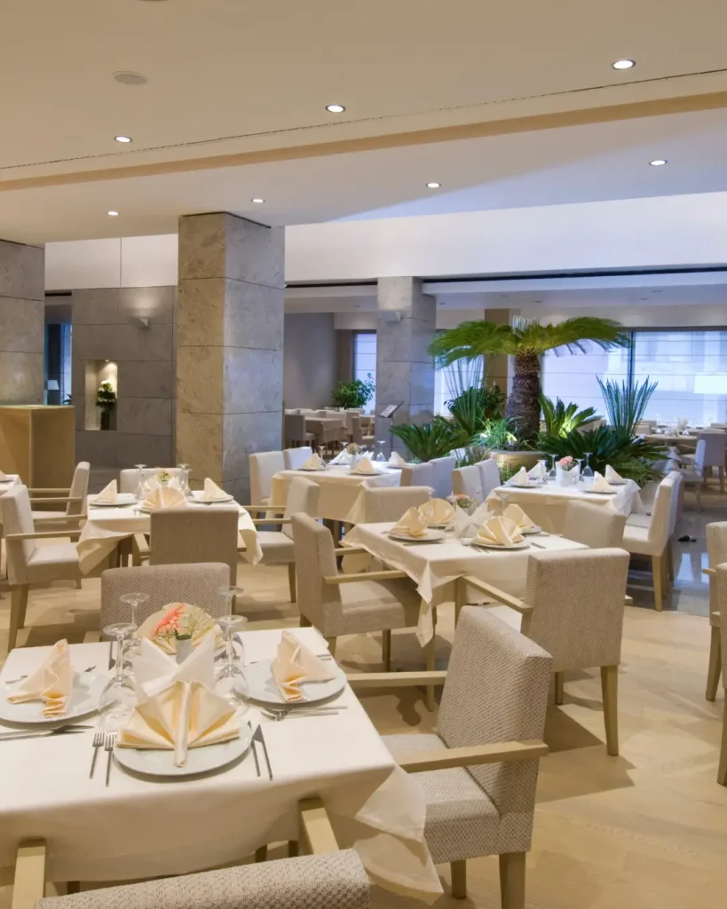 Elegant restaurant interior with neatly set tables, upholstered chairs, and indoor greenery.
