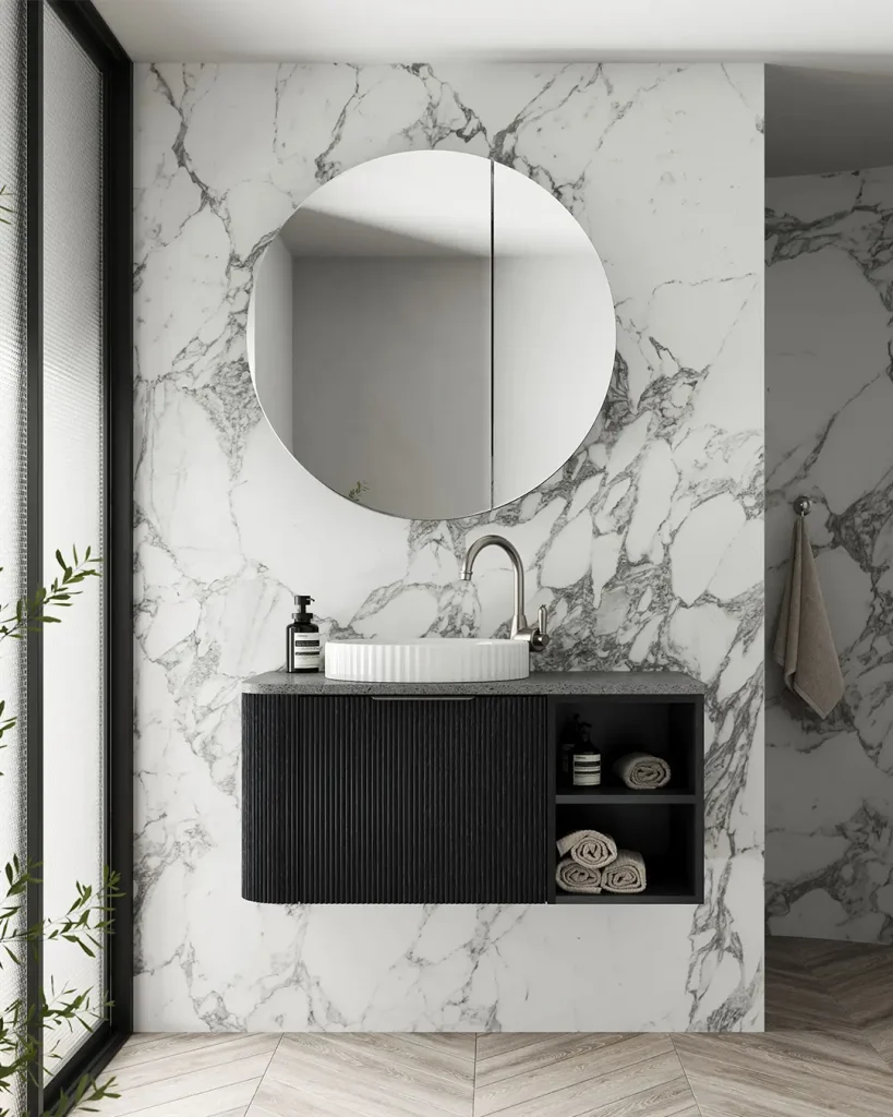 Luxury black fluted vanity with round mirror and textured stone benchtop against full-height marble wall