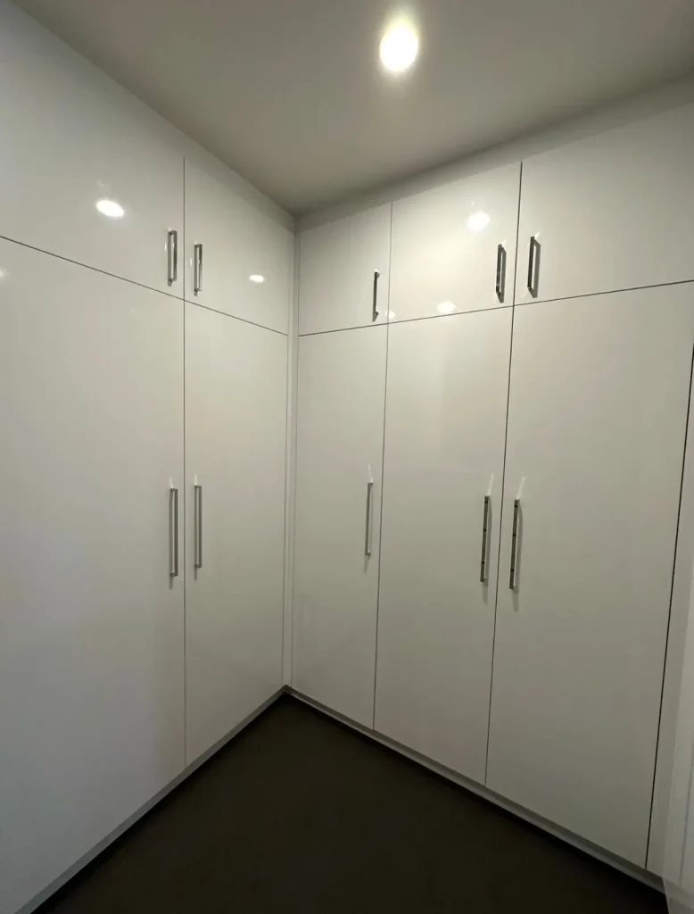 Corner of a room with full-height glossy white built-in cabinets and silver handles.