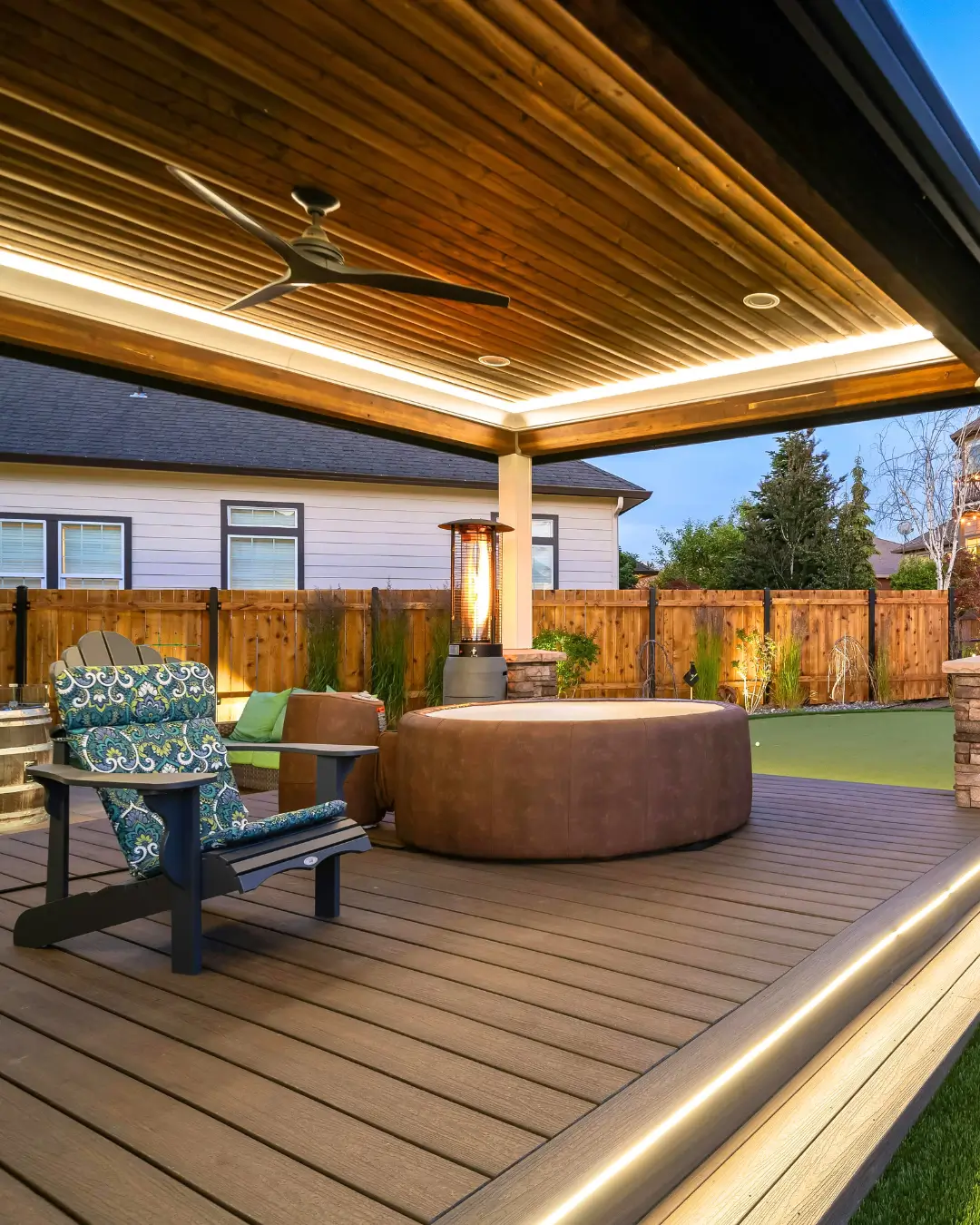 Modern covered deck with ceiling fan, ambient lighting, and circular outdoor spa set against timber fence backdrop.