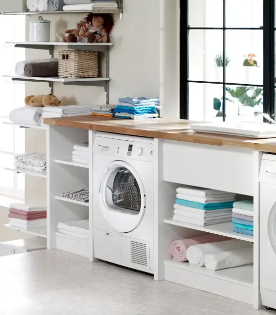 Bright, modern laundry room with under-bench washer and dryer, timber benchtop, open shelving, and large black-framed windows.
