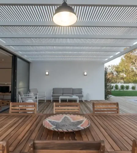 Modern outdoor alfresco area with timber decking, slatted pergola roof, and seamless indoor-outdoor living design, featuring a dining setting, lounge area, and pool.
