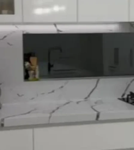 Close-up of a modern kitchen with white marble splashback, mirrored insert, and sleek cabinetry.
