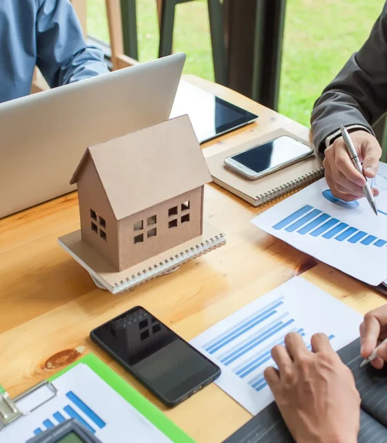 Team reviewing building plans and permit requirements for outdoor living projects beside a miniature house model.