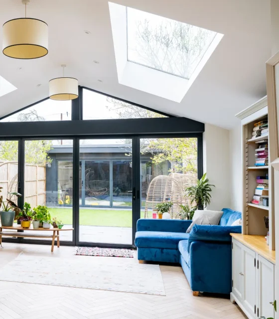 Bright living space with skylights, sliding glass doors, and a blue velvet sofa facing a landscaped backyard.