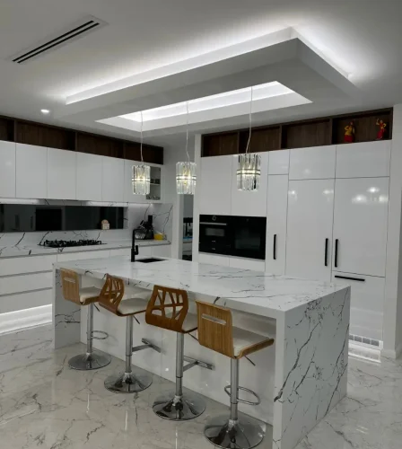 Luxurious white kitchen with marble island, pendant lighting, and integrated appliances.
