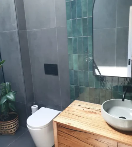 Modern bathroom with green feature tiles, wall-hung toilet, timber vanity, and round basin.