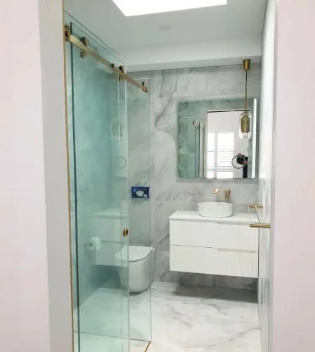 Modern bathroom with marble finishes, floating vanity, glass shower, and gold fixtures.